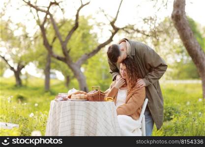 Young couple enjoying food and drinks in beautiful summer green park on romantic date picnic, handsome man and woman with curly hair are hugging outdoors.. Young couple enjoying food and drinks in beautiful summer green park on romantic date picnic, handsome man and woman with curly hair are hugging outdoors