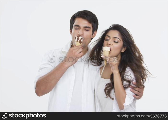 Young couple enjoying ice-cream cones over white background