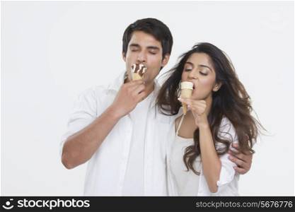 Young couple enjoying ice-cream cones over white background