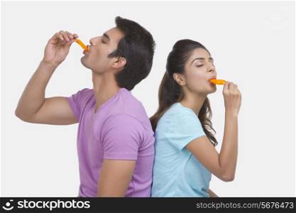 Young couple enjoying orange ice lollies over white background