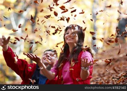 Young couple enjoying the falling leaves in the autumn park