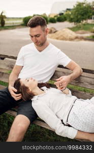 Young couple enjoying time together - woman lying on knees of man on bench on summer sunny day. Smiling man and woman looking on each other.. Young couple enjoying time together - woman lying on knees of man on bench on summer sunny day. Smiling man and woman looking on each other