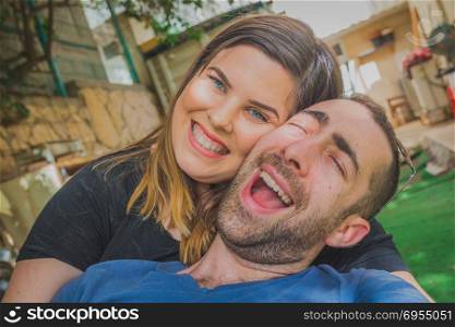 Young couple enjoying together in the backyard. They are smiling, laughing and making funny faces together.