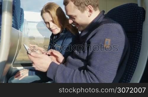 Young couple enjoying train traveling. Together they using tablet computer, laughing and having good time