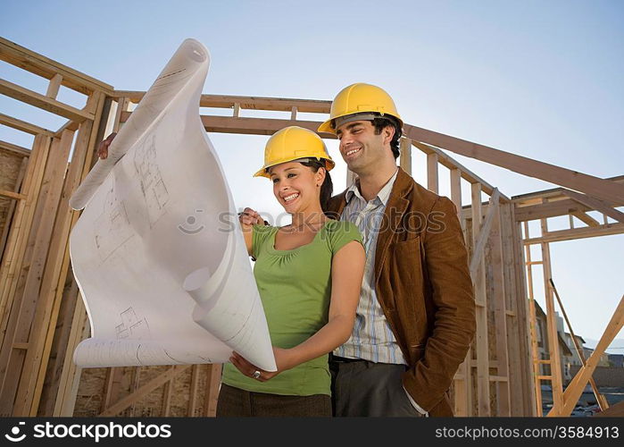 Young couple examining blueprint in construction site