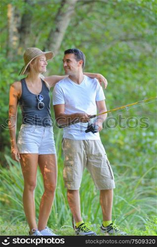 young couple fishing on river shore in grass