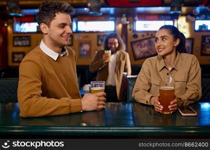 Young couple flirting and drinking beer sitting at sport bar counter. Handsome stranger, nice conversation of young people in pub. Young couple flirting and drinking beer in bar