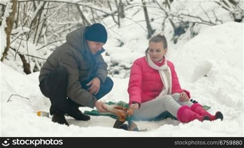 Young couple frying sausages on a fire in the winter forest