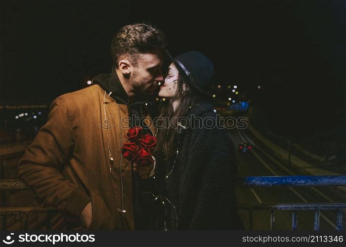 young couple garland kissing dark street