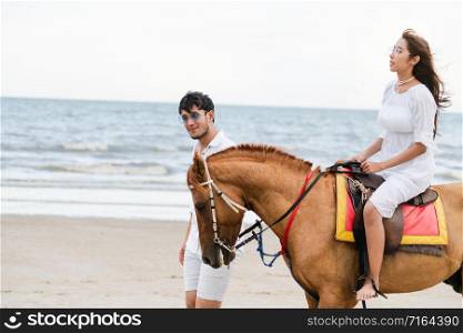 Young couple goes honeymoon horse riding on the beach in summer vacation.. Young couple goes horse riding on tropical beach.