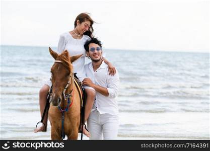 Young couple goes honeymoon horse riding on the beach in summer vacation.. Young couple goes horse riding on tropical beach.
