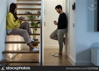 young couple having a cup of coffee in different parts of the house. concept of couple?s incommunication