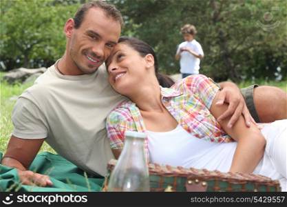 Young couple having a picnic with little boy in the background