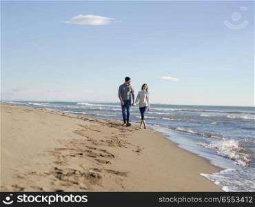 Young couple having fun walking and hugging on beach during autumn sunny day. Loving young couple on a beach at autumn sunny day