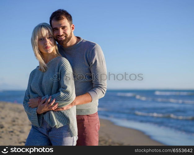 Young couple having fun walking and hugging on beach during autumn sunny day. Loving young couple on a beach at autumn sunny day