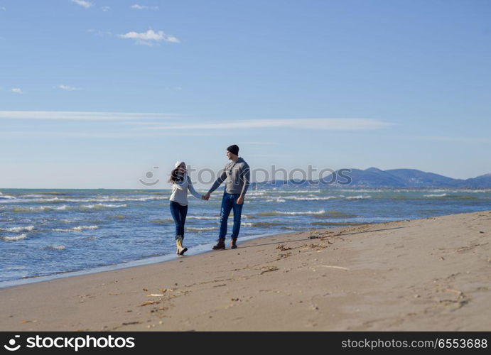 Young couple having fun walking and hugging on beach during autumn sunny day. Loving young couple on a beach at autumn sunny day