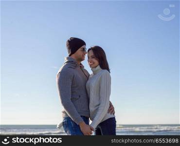 Young couple having fun walking and hugging on beach during autumn sunny day. Loving young couple on a beach at autumn sunny day