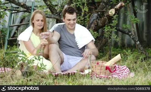 Young couple having picnic in the courtyard. They toasting, drinking wine and talking. Happy romantic moments