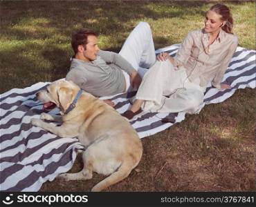 young couple having rest with dog in bloomy garden