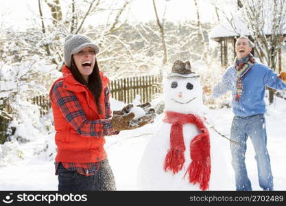 Young Couple Having Snowball Fight In Garden