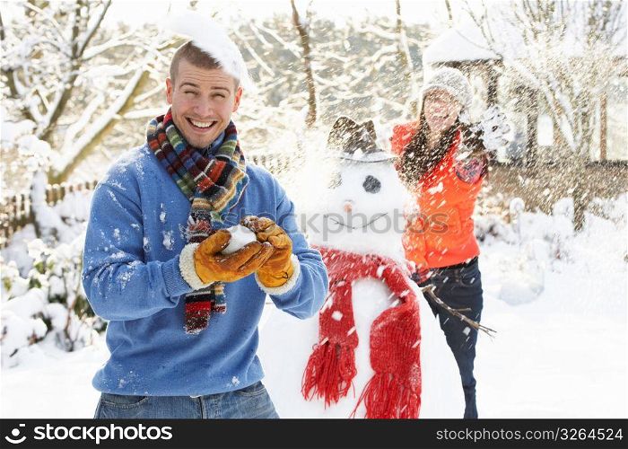 Young Couple Having Snowball Fight In Garden