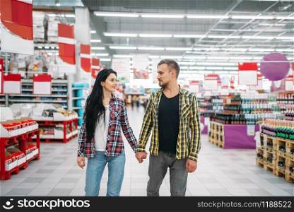 Young couple hold hands in supermarket. Male and female customers on family shopping. Man and woman purchasing in hypermarket. Young couple hold hands in supermarket, back view
