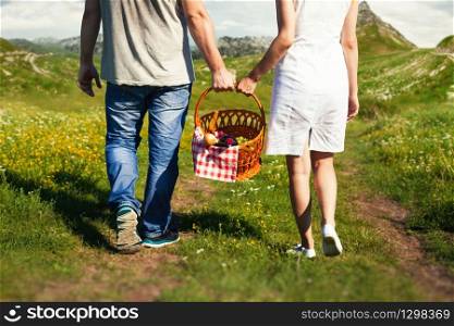Young couple holding a basket walking in nature. Young couple going with picnic basket