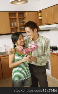 Young couple holding a flower vase and looking at each other in the kitchen