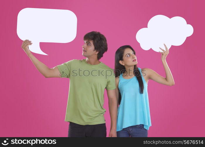 Young couple holding communication bubbles against pink background