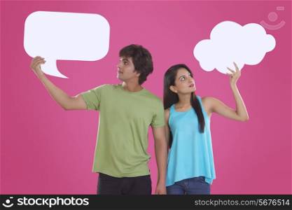 Young couple holding communication bubbles against pink background