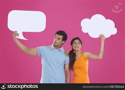 Young couple holding communication bubbles against pink background