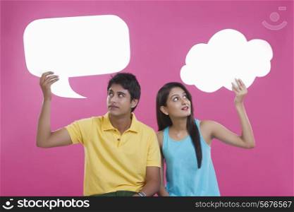 Young couple holding communication bubbles over pink background