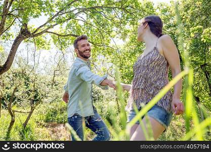 Young couple holding hands in forest fooling around smiling