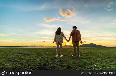 young couple holding hands in green field at sunset