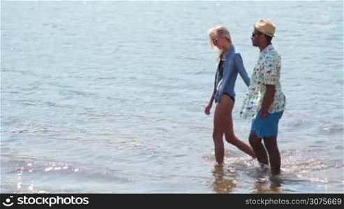 Young couple holding hands walking romantic in the waters edge on the beach on vacation travel holidays