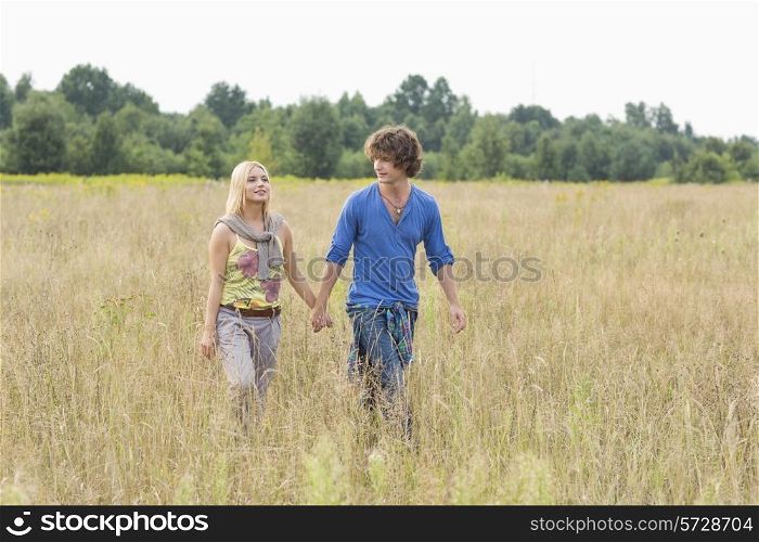 Young couple holding hands while walking through field