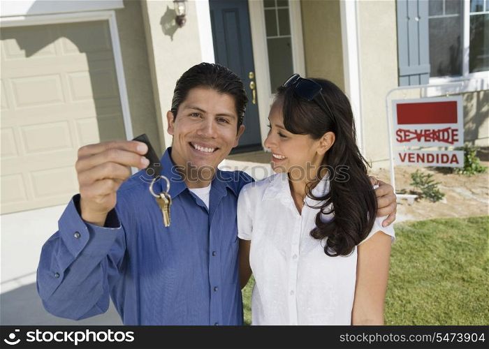 Young couple holding keys outside new home, portrait