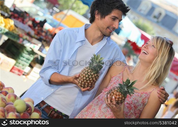 Young couple holding pineapples at a market stall
