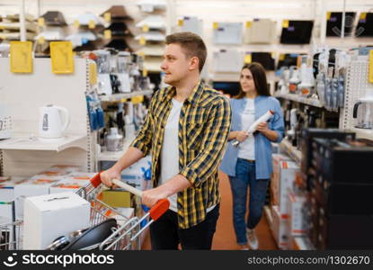 Young couple holds electric blender in electronics store. Man and woman buying home electrical appliances in market. Couple holds electric blender in electronics store