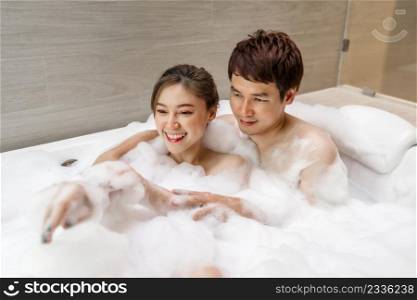 young couple hugging and washing body with foam in bathtub