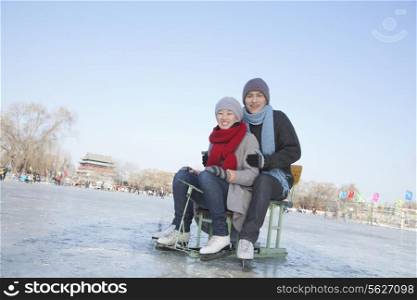 Young Couple Ice Skating, Sitting on Ice Sled