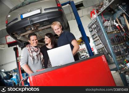 Young couple in auto repair shop standing with mechanic looking at laptop