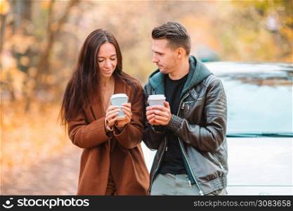 Young couple in autumn with coffee on car vacation. Happy family walking in autumn park on sunny fall day