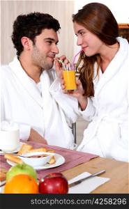 young couple in bathrobe drinking orange juice out of straw