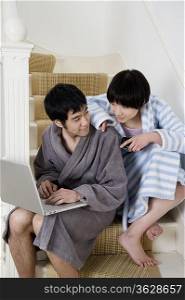 Young couple in bathrobe sitting on stairway with laptop