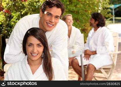 Young couple in bathrobes sitting on a terrace with friends