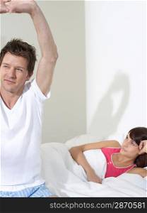 Young couple in bed woman sitting up man stretching
