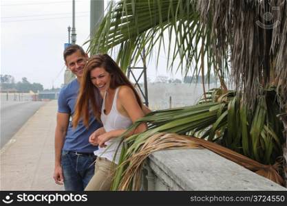 Young couple in front of a palm tree on a bridge.