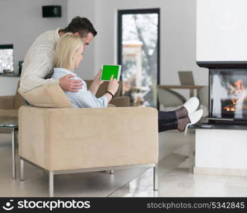 Young Couple in front of fireplace surfing internet using digital tablet on cold winter day at home