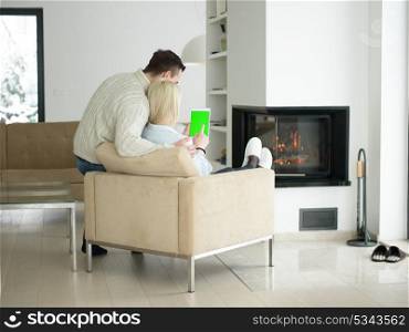 Young Couple in front of fireplace surfing internet using digital tablet on cold winter day at home